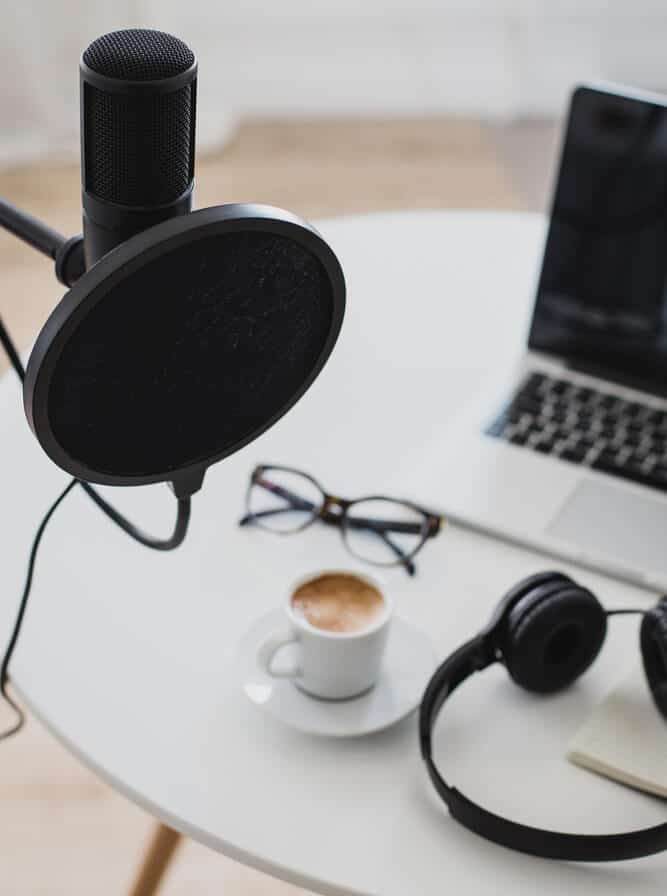 podcast microphone in front of table with computer, headphones, and coffee